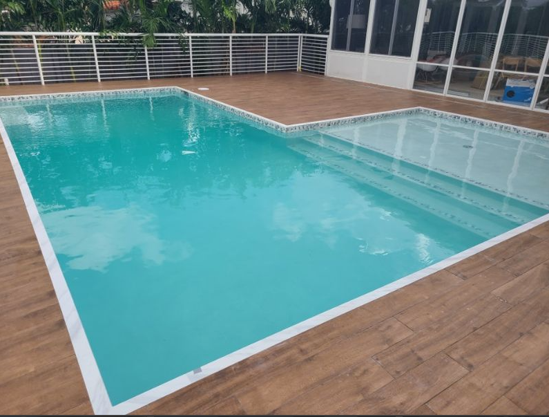 A large swimming pool with a wooden deck in front of a screened in porch.