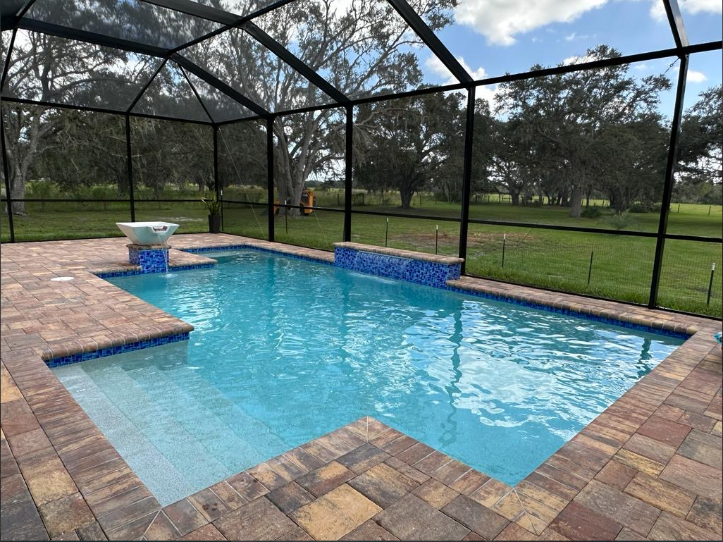A large swimming pool is surrounded by a screened in area.