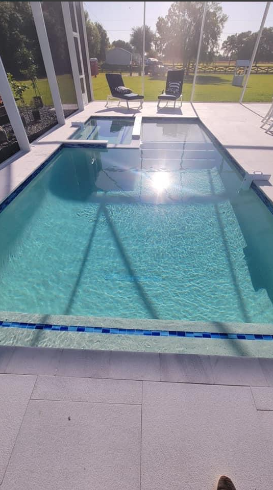 A large swimming pool is surrounded by chairs and a screened in porch.