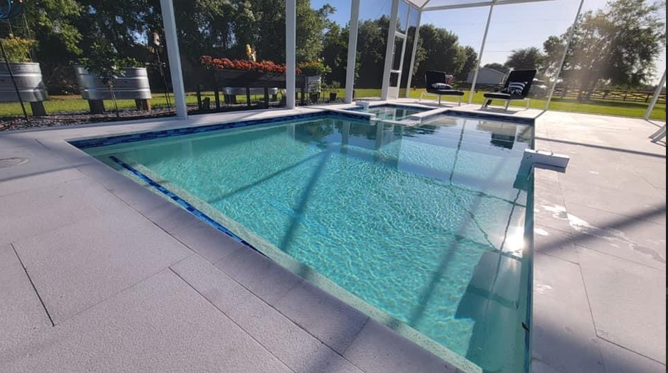 A large swimming pool is surrounded by a screened in area.