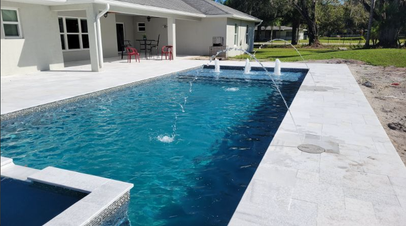A large swimming pool with a fountain in the middle of it in front of a house.