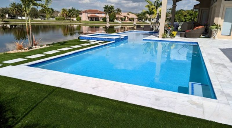 A large swimming pool in the backyard of a house next to a lake.