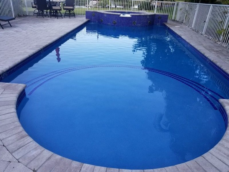 A large blue swimming pool with a table and chairs in the background.
