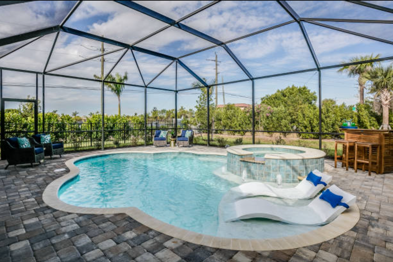 There is a large swimming pool in the middle of a screened in area.