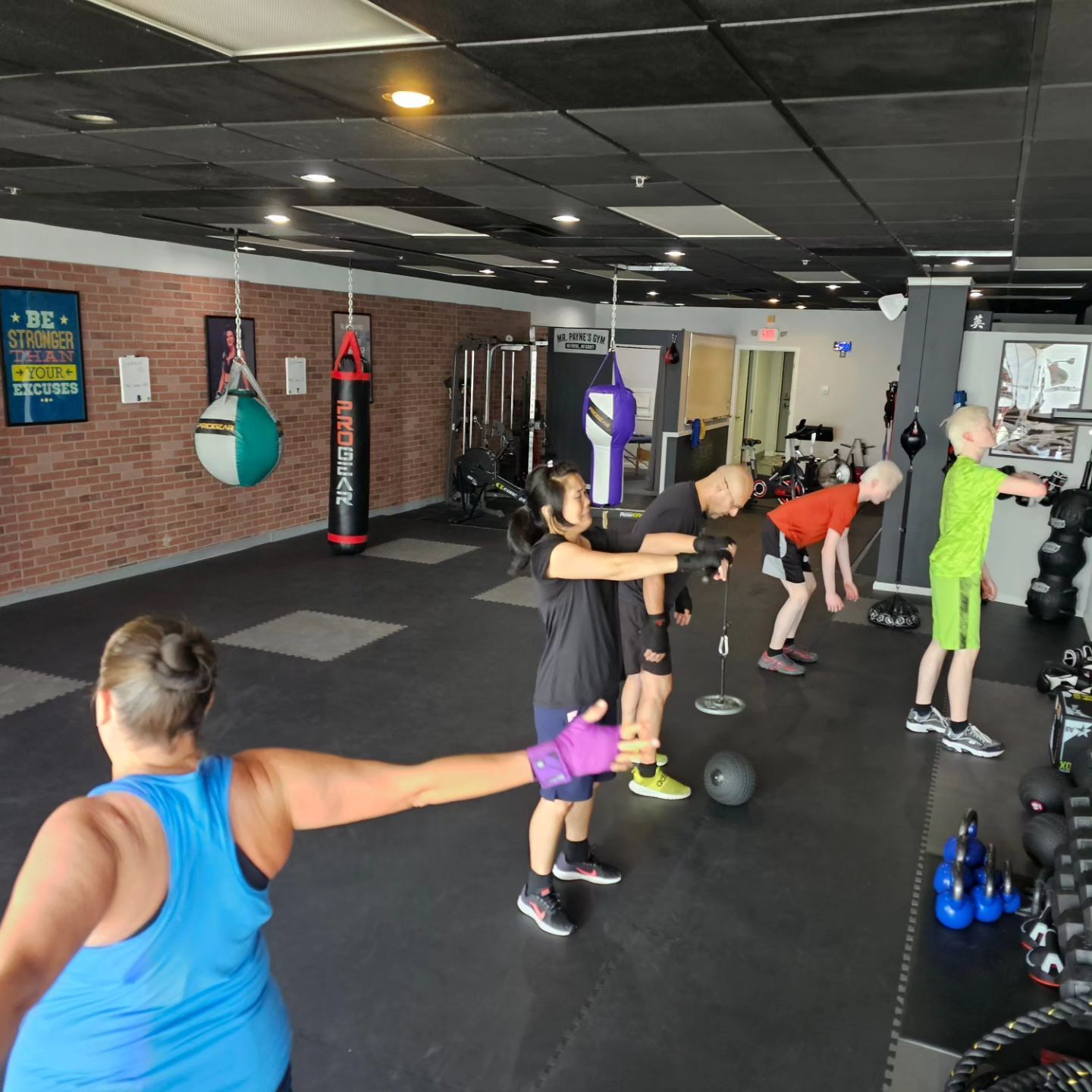 People exercising in a gym with weights and punching bags. One woman reaches outward, others bend over with equipment.