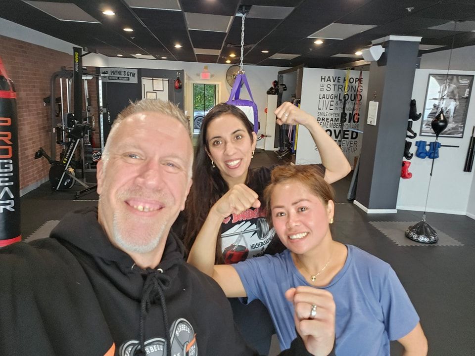 Three people in a gym smiling and flexing their muscles. Man takes selfie, women show strength.