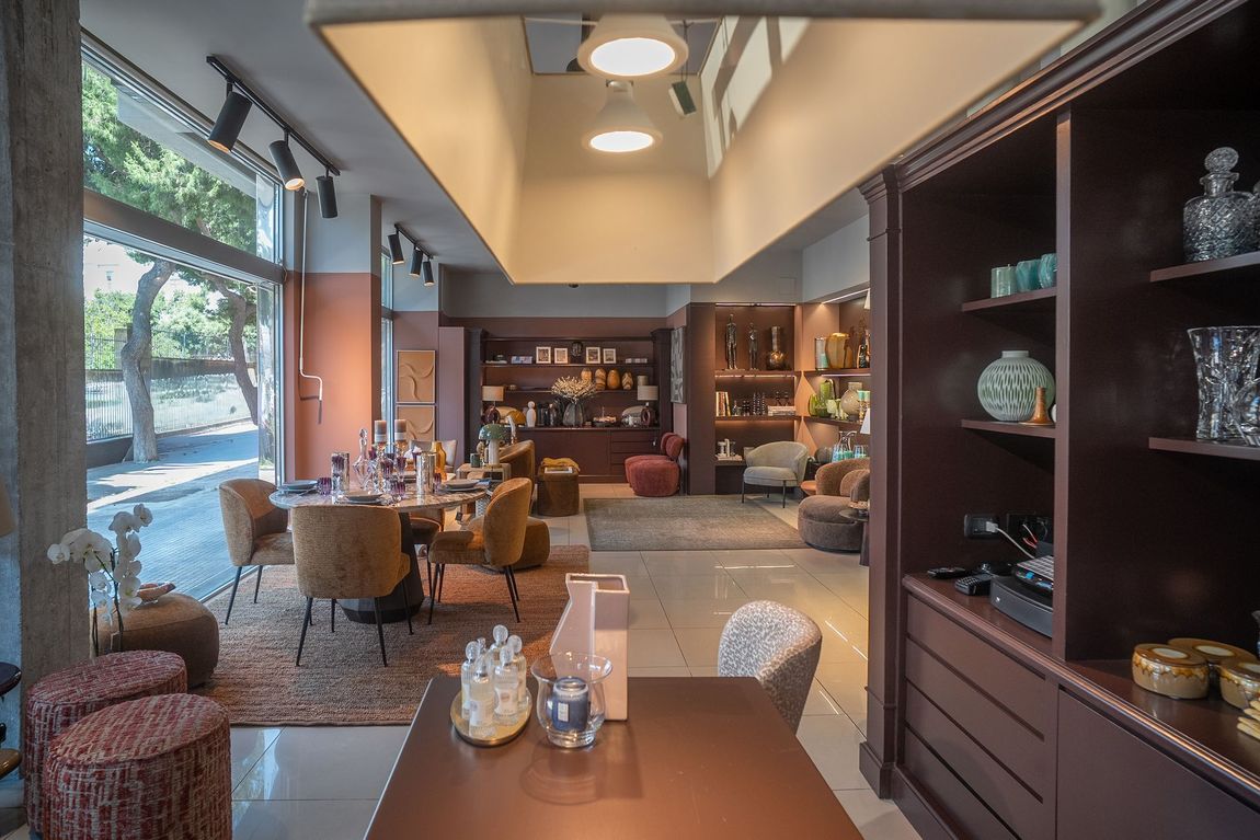 Interni moderni di un caffè con tavoli, sedie, scaffali e una luce calda proveniente dalle ampie finestre.