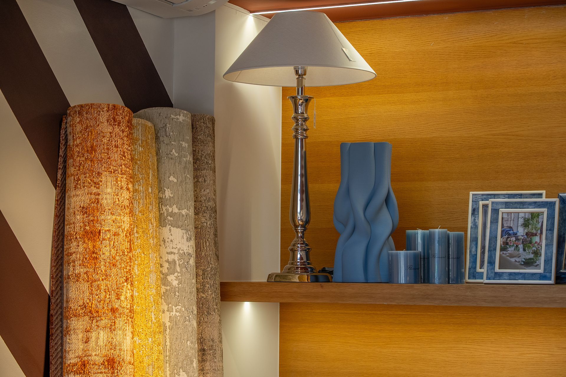 Mensola in legno con lampada, vaso blu, libri impilati e foto incorniciate accanto a tende tessute.
