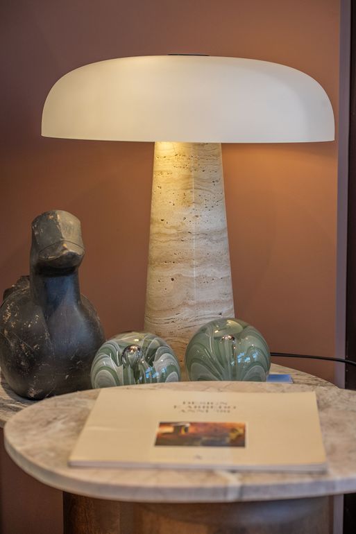 Lampada da tavolo su un tavolino rotondo con oggetti decorativi e un libro, contro una parete dai toni caldi.