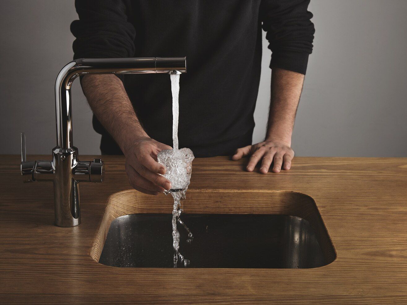A man is washing a glass in a kitchen sink