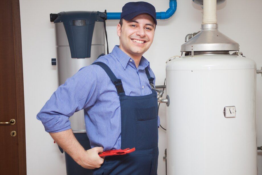 A man is standing in front of a water heater holding a wrench.