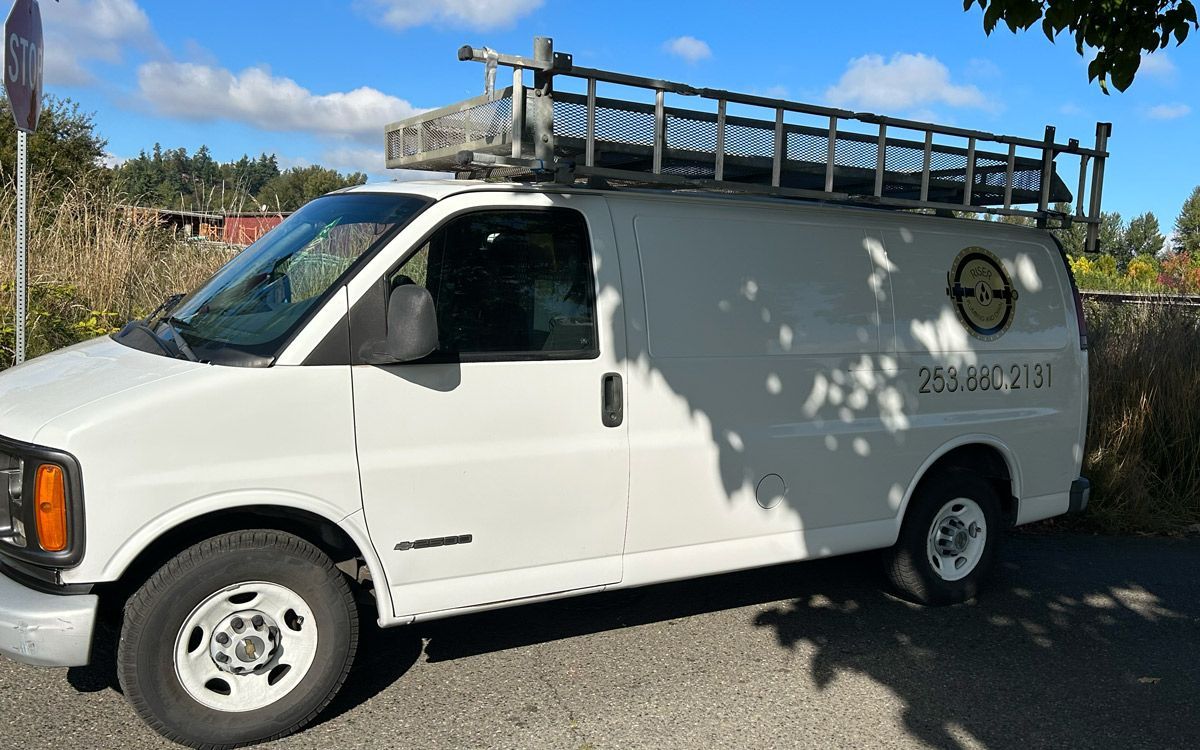 A white van with a ladder on top of it is parked on the side of the road.