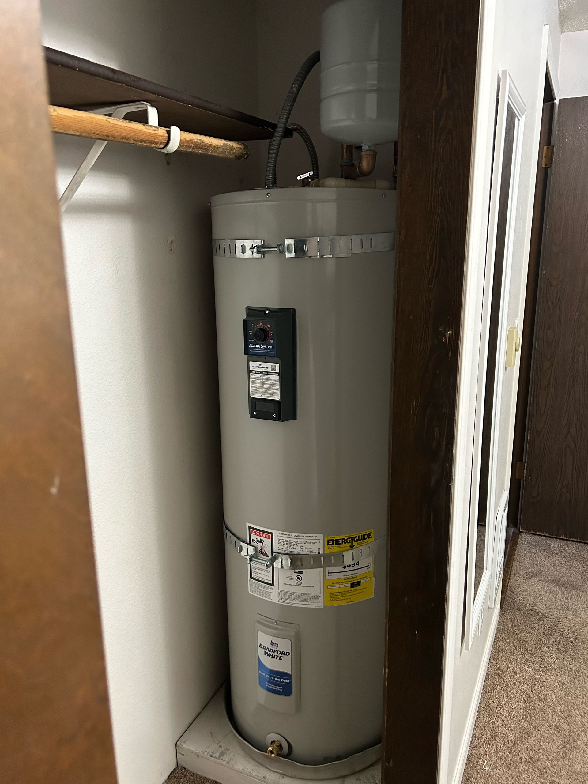 A water heater is sitting in a closet next to a wall.