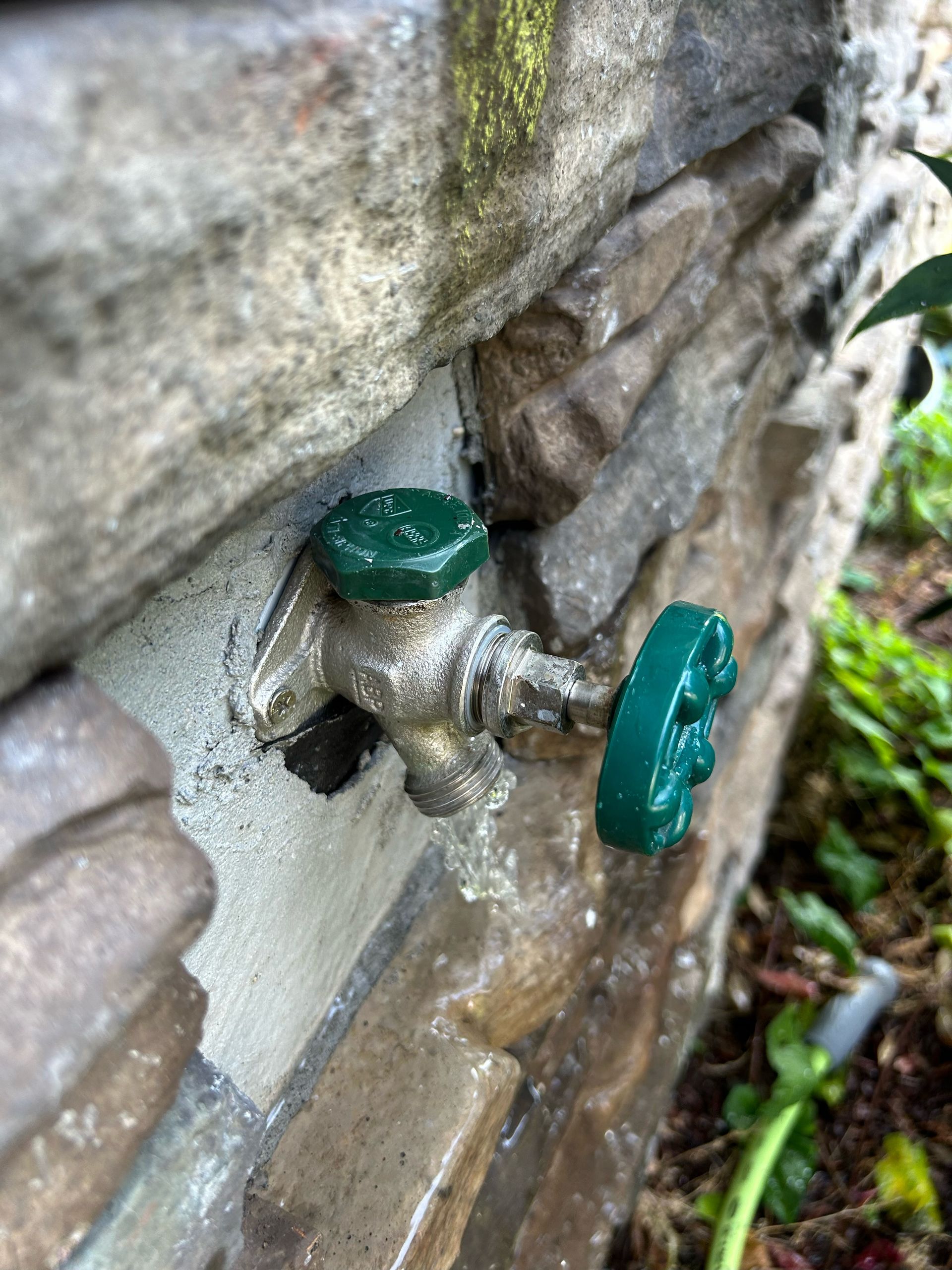 A faucet with a green handle is attached to a stone wall.