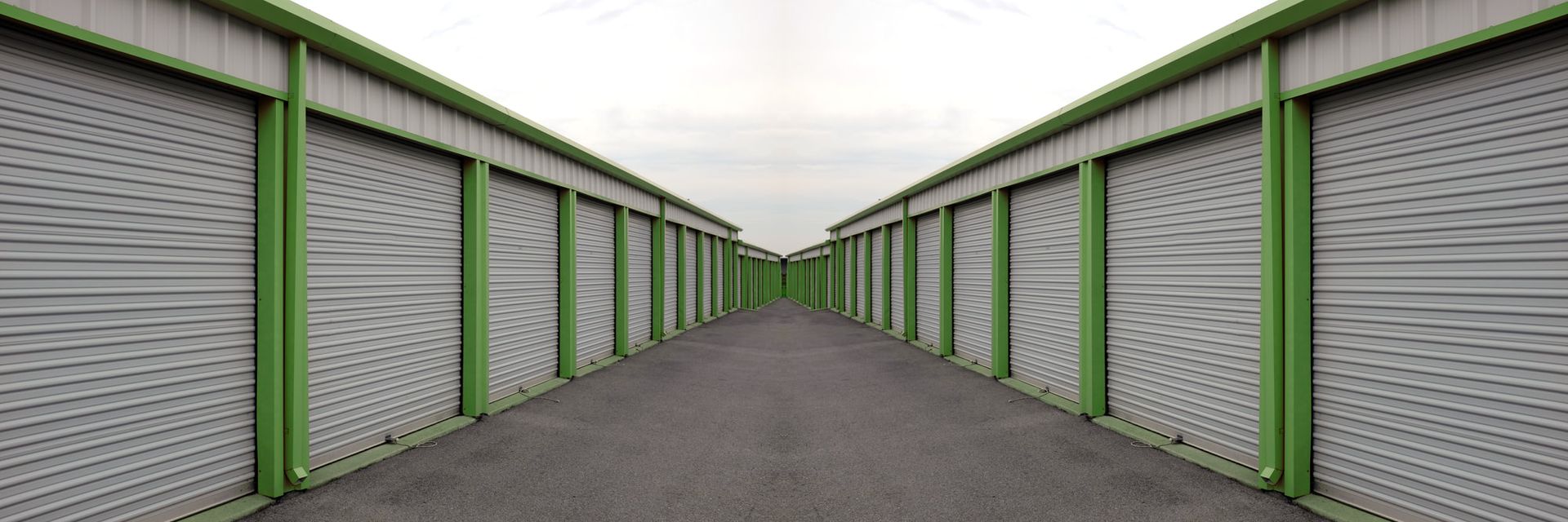 Storage units in a long, gray corridor, with green support beams, and an overcast sky.