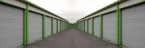 Storage units in a long, gray corridor, with green support beams, and an overcast sky.