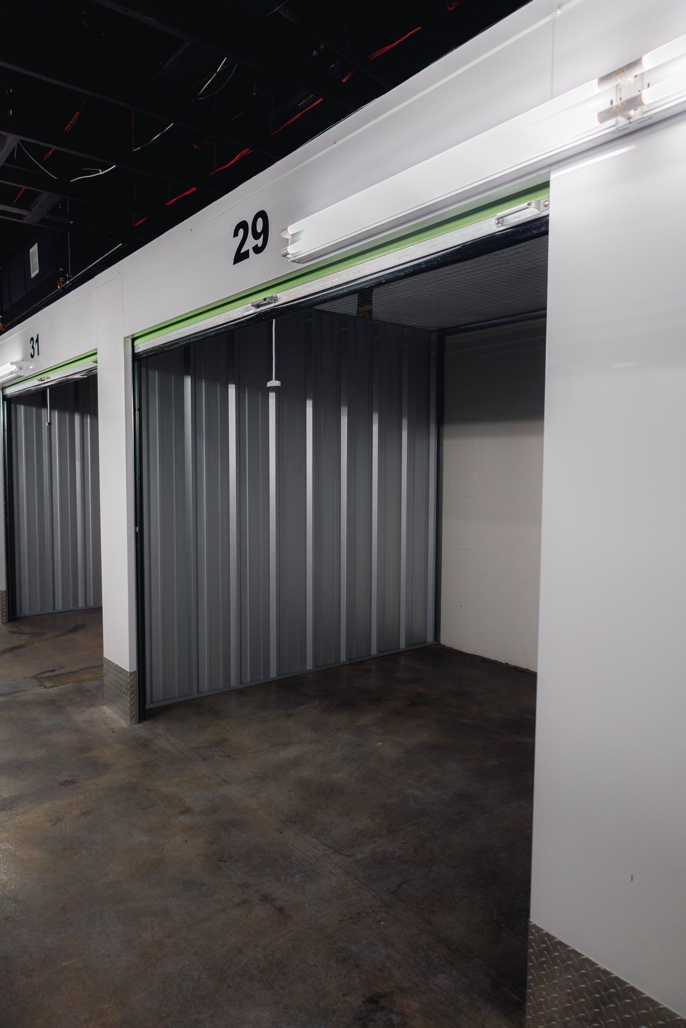 Empty storage units, one open, in a dim interior. Unit numbers visible above the doorways.