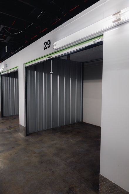 Empty storage units, one open, in a dim interior. Unit numbers visible above the doorways.