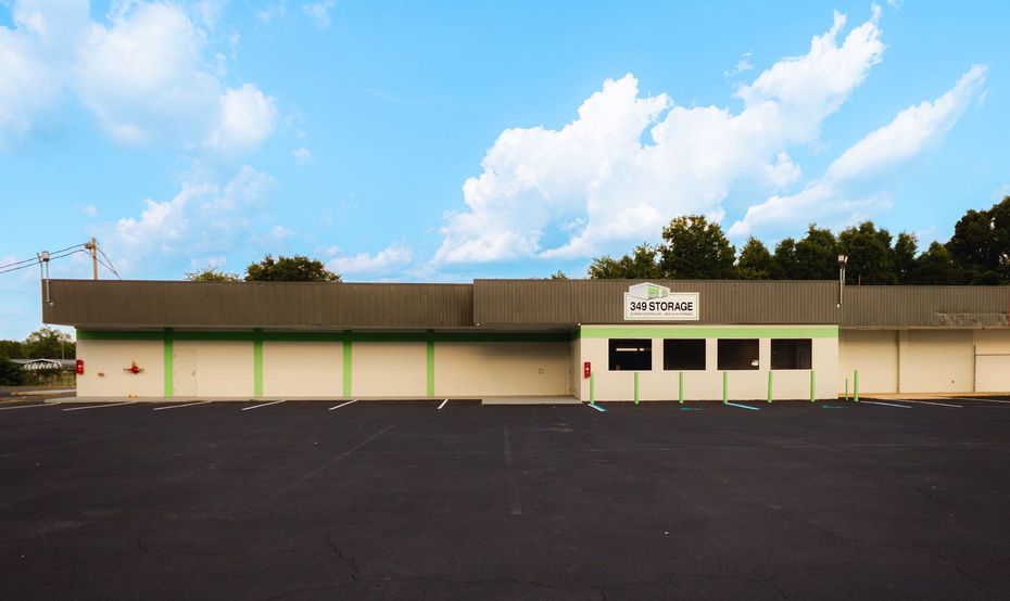 A building with green and grey accents sits under a blue sky. The structure has a black parking lot in front.