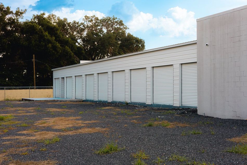 White storage units in a row, gravel ground, trees in the background, bright sky.