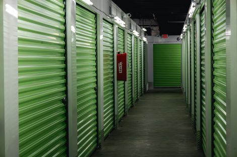 A hallway of green storage units in an indoor facility. A red fire extinguisher is mounted on a wall.