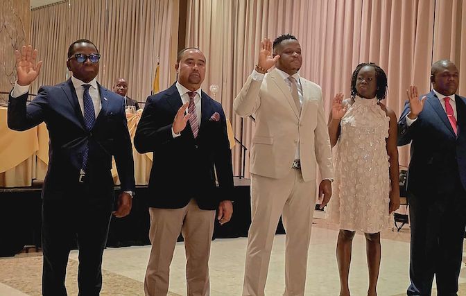 Five people raising their right hands, taking an oath. Formal setting with gold and beige decor.