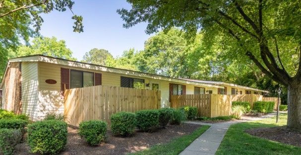 Row of tan townhomes with brown doors, wooden fences, and green landscaping.