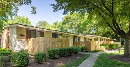 Row of tan townhomes with brown doors, wooden fences, and green landscaping.