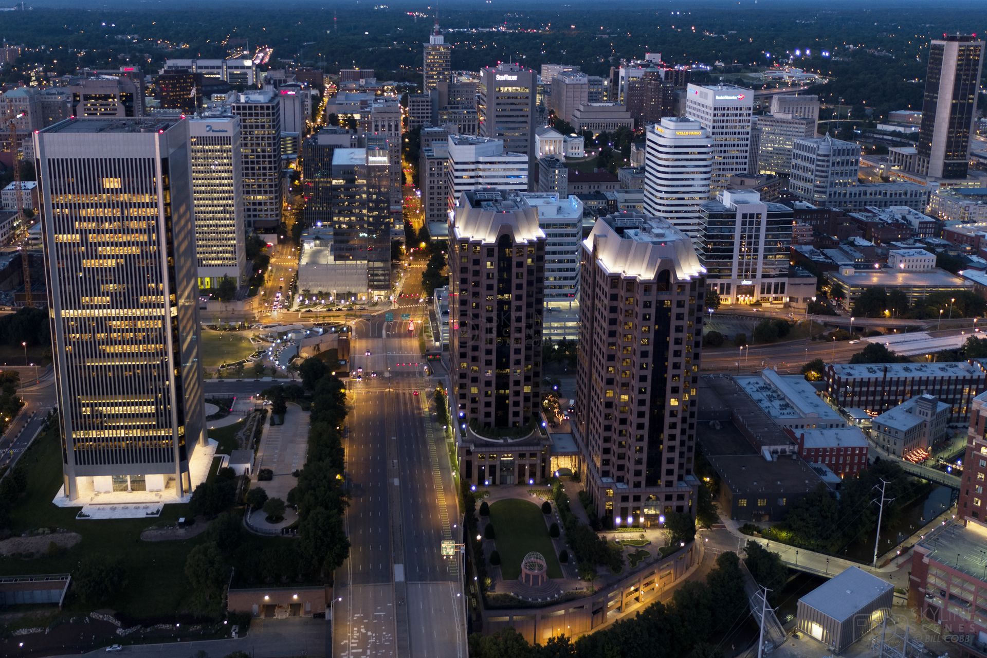 Aerial view of a city skyline at dusk with lit buildings and streetlights.