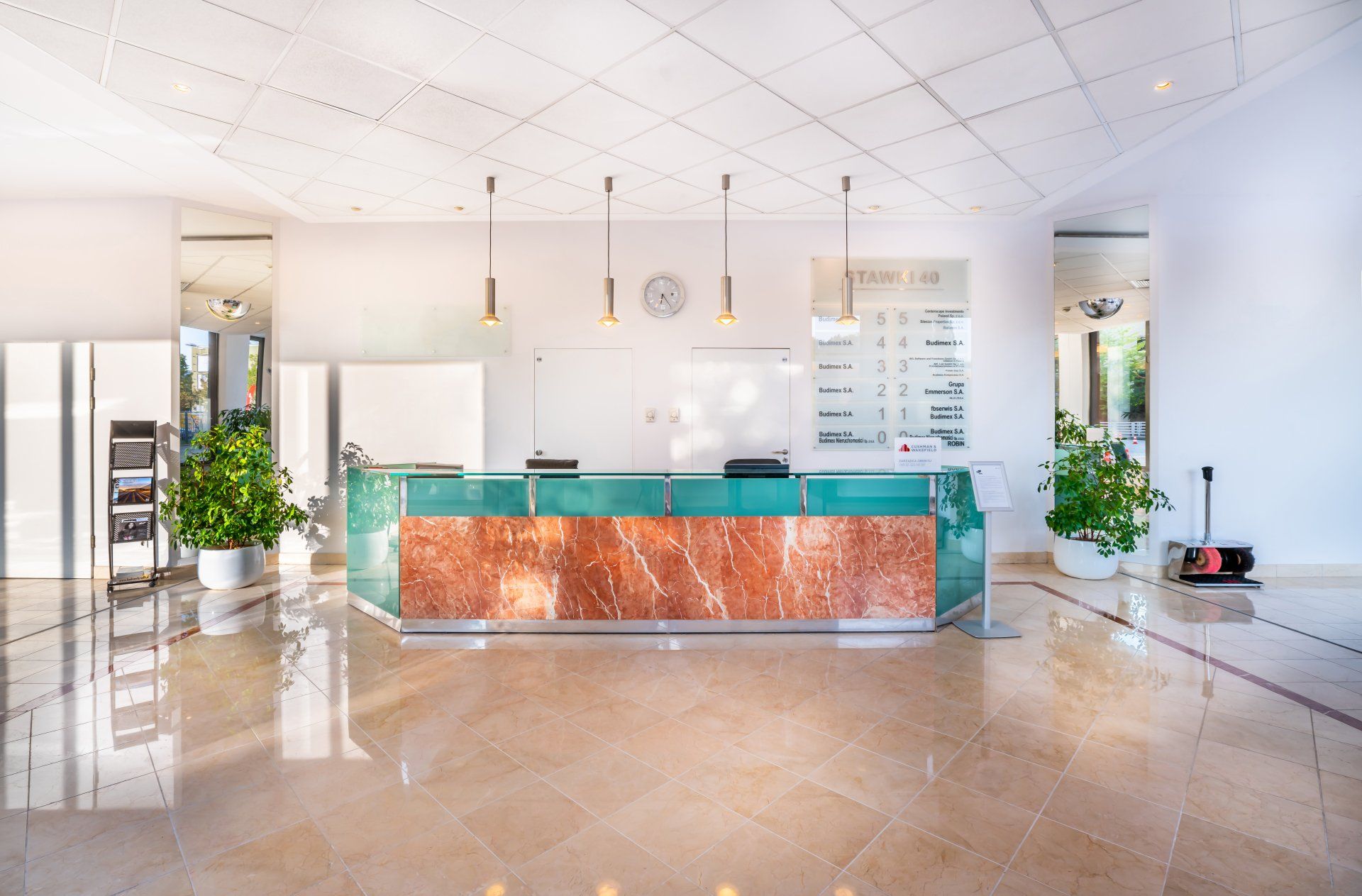 Recepcja z marmurowym frontem i szklanym blatem w jasnym holu.