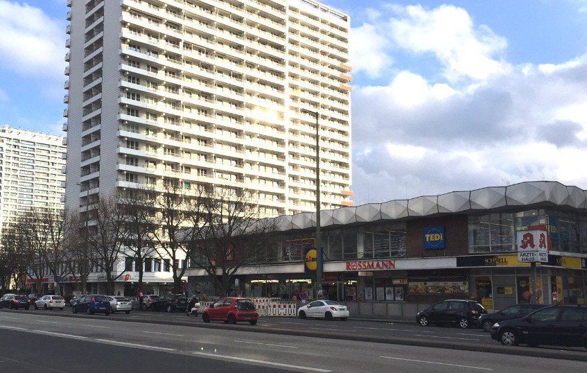Tall apartment buildings and a shopping area with a Lidl supermarket and pharmacy on a sunny day.