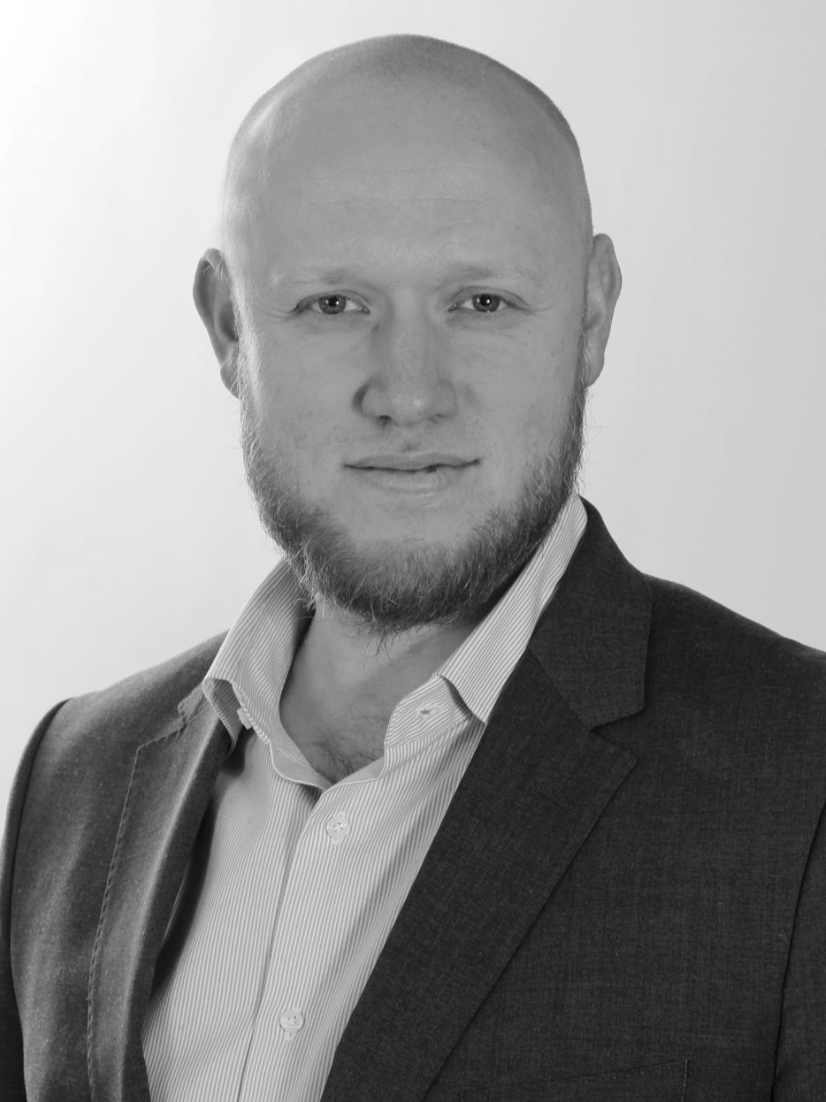 Lächelnder Mann in Anzug und Krawatte posiert für ein professionelles Porträtfoto.