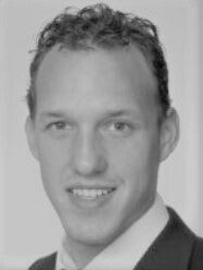 Mann im Anzug lächelt in die Kamera, mit kurzen dunklen Haaren und heller Haut.