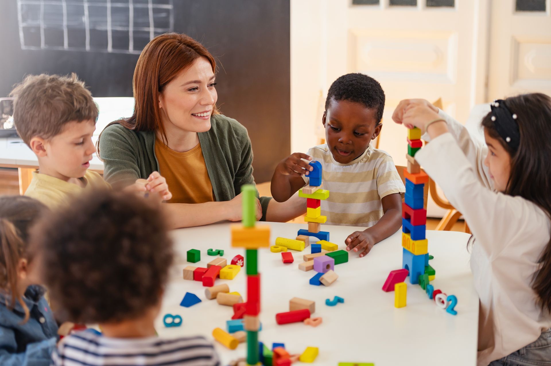 A teacher is watching some kids play with building blocks.