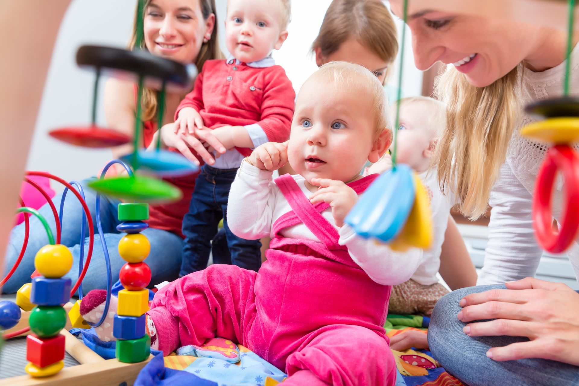 Portrait of a cute baby girl while sitting down on the floor with two other babies and their carers.