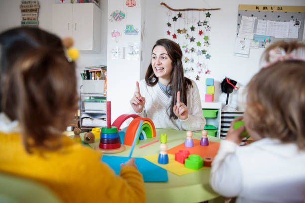 Teacher interacting with children at a colorful classroom table.