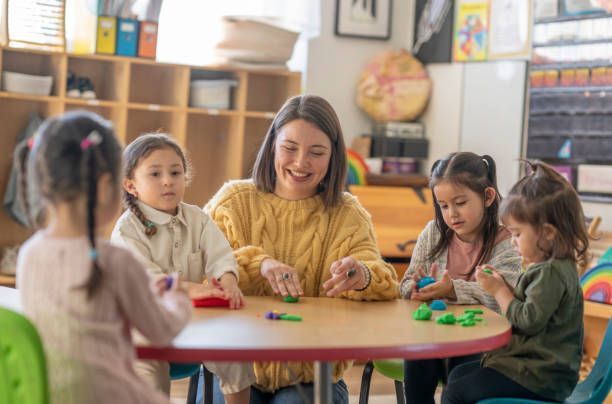 Teacher and kids playing with clay at a round classroom table.