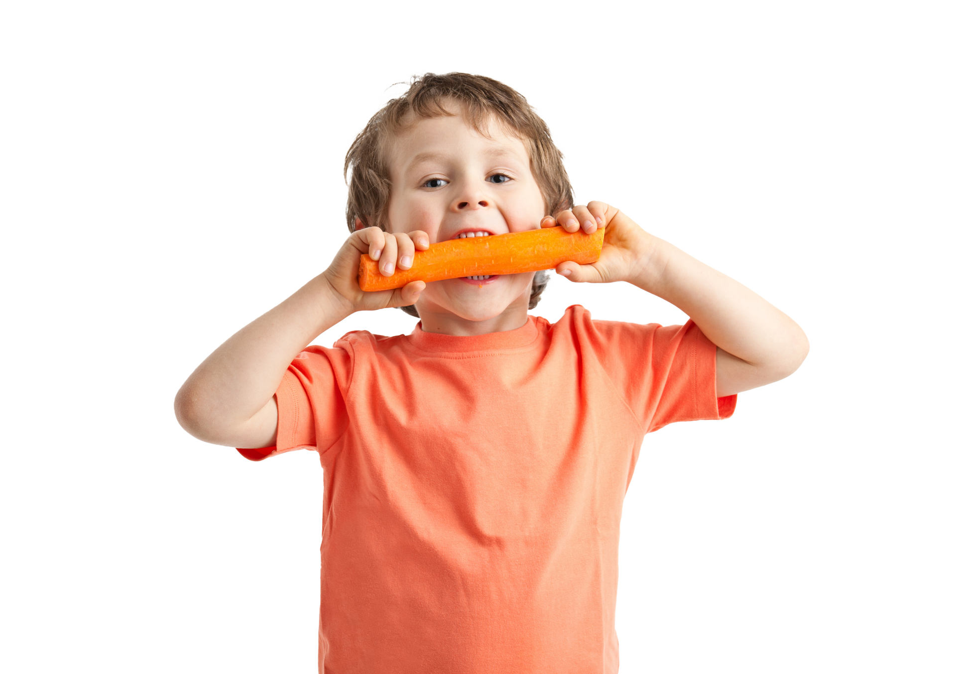 Boy eating a carrot, smiling, wearing an orange shirt, against a white background.