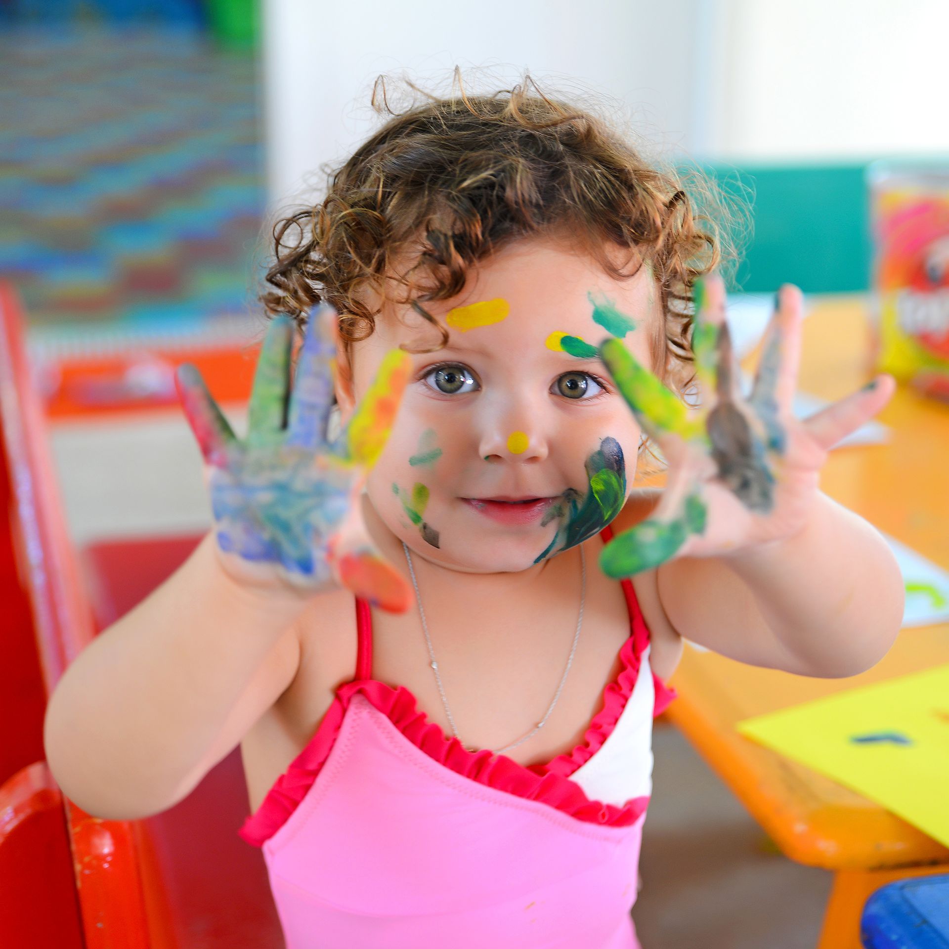 Child showing colorful paint-covered hands during creative preschool art activity.