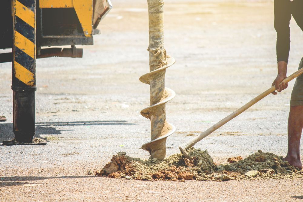 A Man Is Using A Drill To Dig A Hole In The Ground — Territory Industries Pty Ltd In Katherine, NT