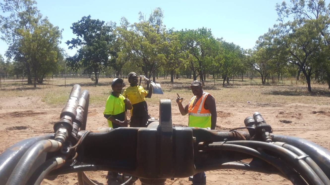A Group Of Men Are Standing In A Field With Trees In The Background — Territory Industries Pty Ltd In Larrimah, NT