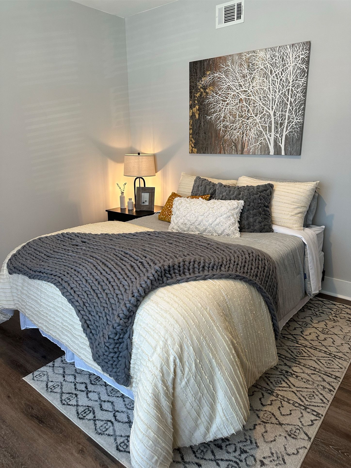 A bedroom with a bed , nightstand , lamp and painting on the wall.