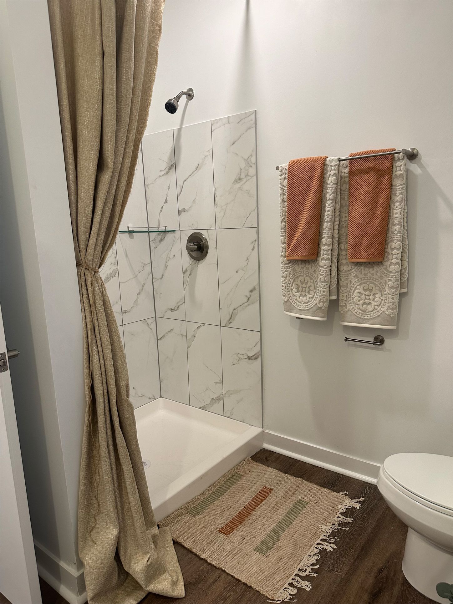 A bathroom with a toilet , shower , and towels hanging on the wall.