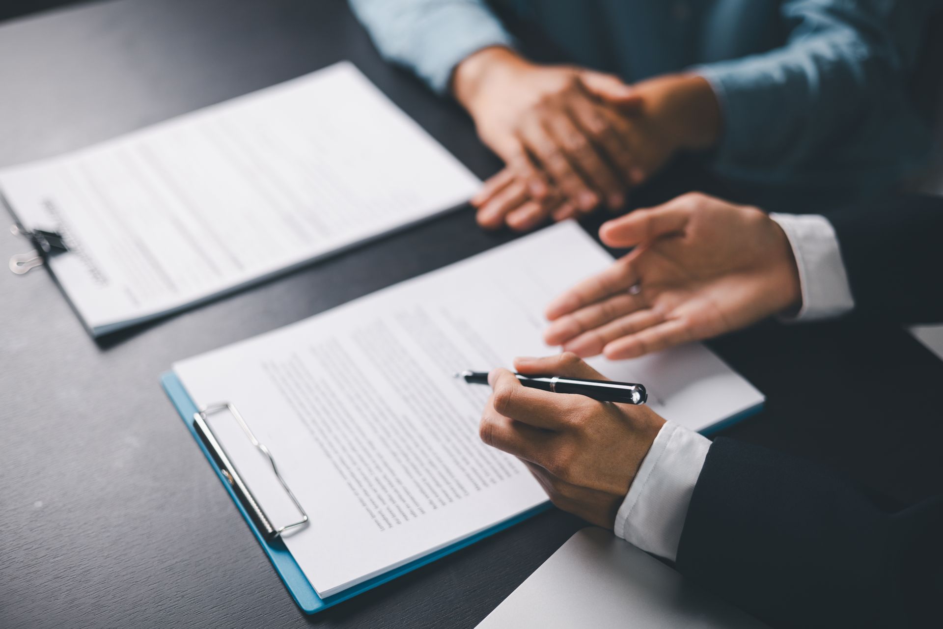 Two people at a desk reviewing legal documents, with one person pointing to a contract while holding a pen.
