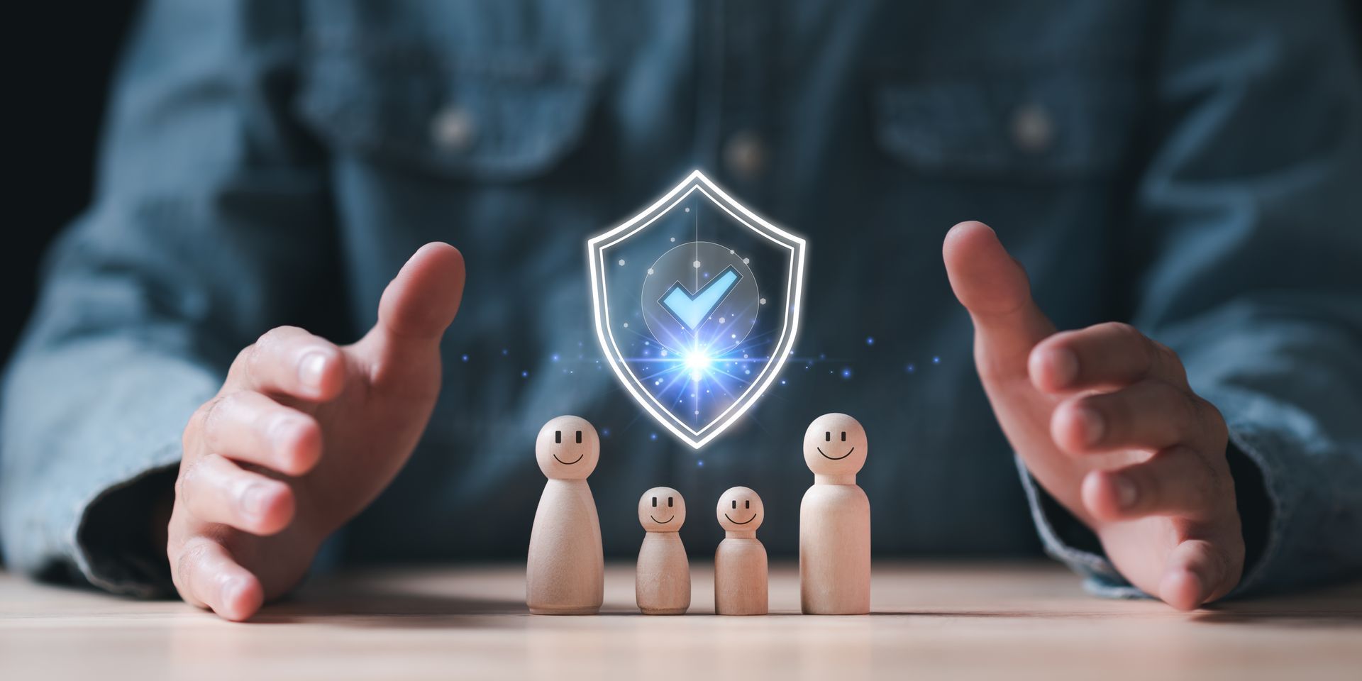 A person's hands cup four wooden figures protected by a glowing digital shield icon with a checkmark.