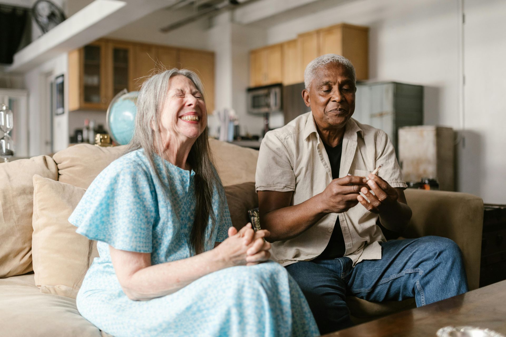 A couple sitting together on a couch, smiling and laughing in a bright, indoor living space.