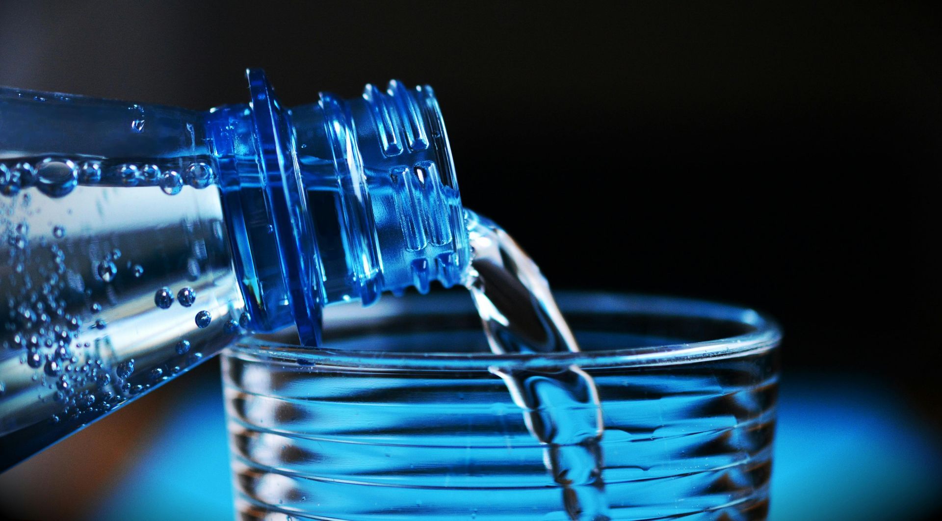 Water pouring from a blue plastic bottle into a clear glass.