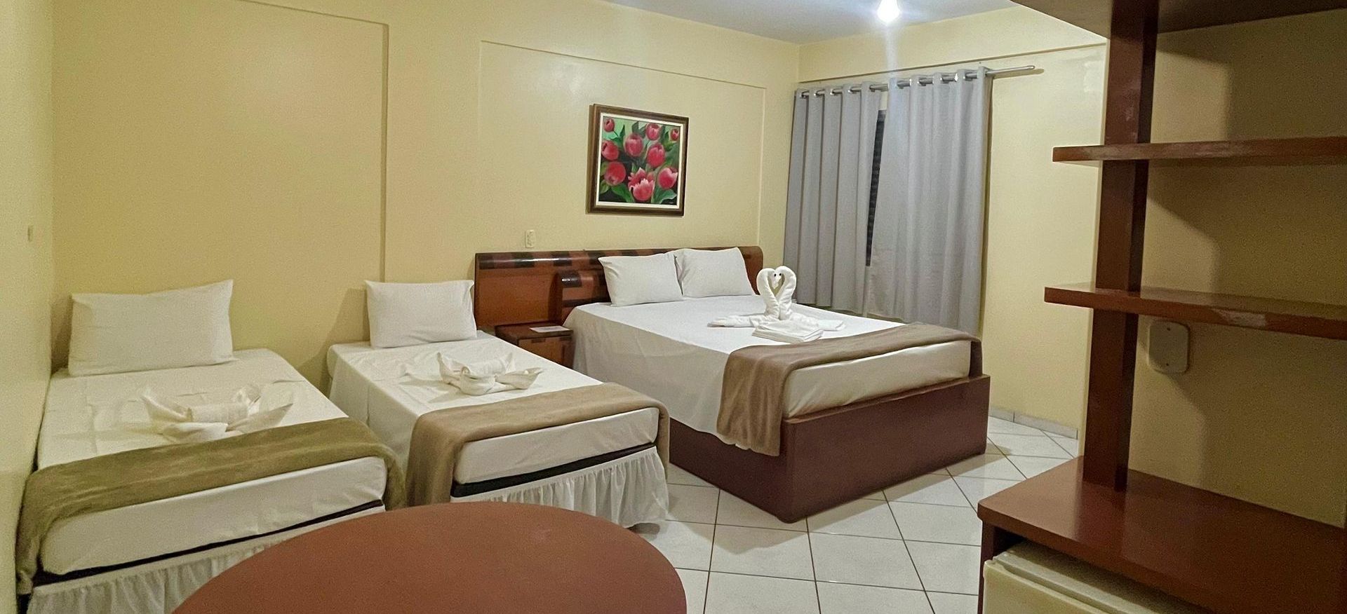 Um quarto de hotel com três camas e uma mesa.