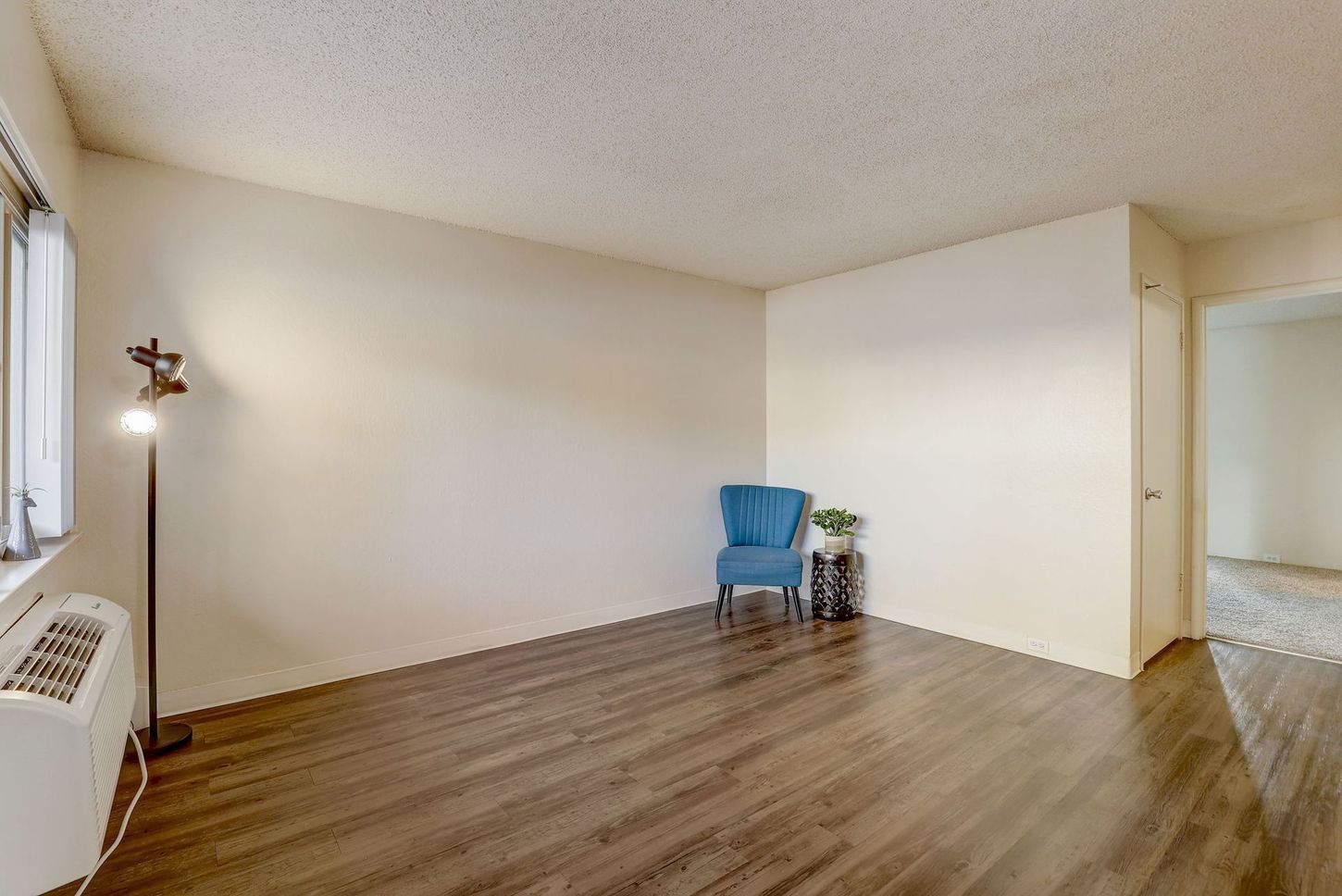 A living room with hardwood floors , a blue chair , a lamp and a window.