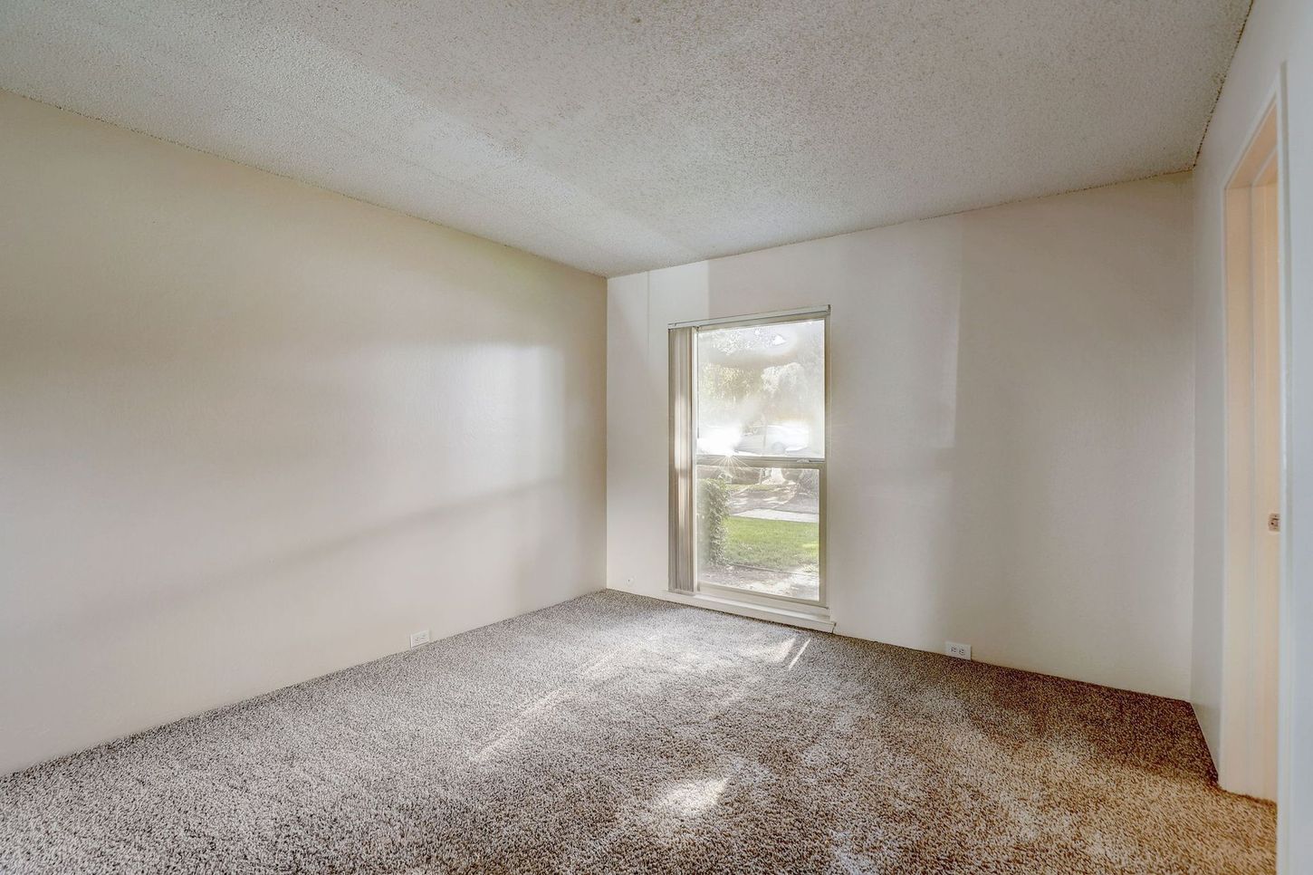 An empty bedroom with a carpeted floor and a window.